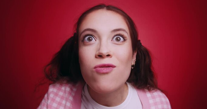 Close up of amazed young woman with funny face and popeyes surprised watching tv cinema show commercial content on a big screen, eating popcorn isolated on red studio background. Wow effect concept