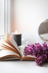 Spring flatlay at home with lilac, book and candle. Season blooming time.