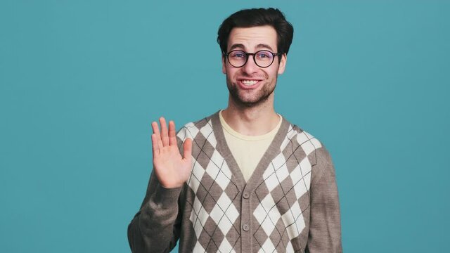 The happy man with glasses waving at the camera while standing in the blue studio