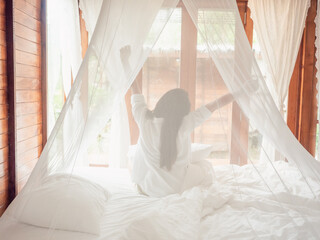 Backside of Woman stretching in bed after wake up, Happy greets new day with warm sunlight.