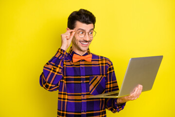 Photo of young cheerful man happy positive smile look laptop watch seminar isolated over yellow color background