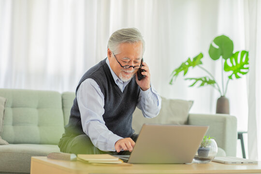 Happiness Asian Senior Handsome Business Man With White Hairs Hold Mobile Phone And Using Computer Laptop Talking With Business Team And Meeting Online Video Conference Working At Home