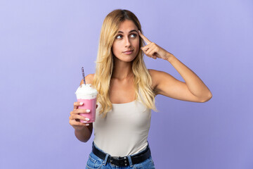 Young blonde Uruguayan woman with strawberry milkshake isolated on purple background having doubts and thinking