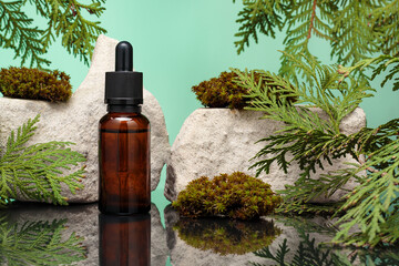 Glass bottle of essential oil among leaves of white cedar and moss against green background. Essence liquid for skin care or alternative medicine.