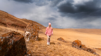 a girl with a dog walks on a mountain next to large rocks white labrador