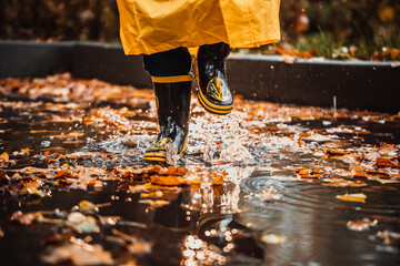 the child jumps into a puddle. legs in yellow rubber boots.