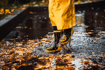the child jumps into a puddle. legs in yellow rubber boots.
