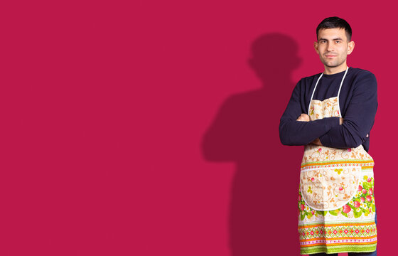 Banner, red background. Caucasian brunette young handsome chef man, in colorful apron crossed arms looking confident at the camera. Plenty space for ad your information text. Man ready to cooking .
