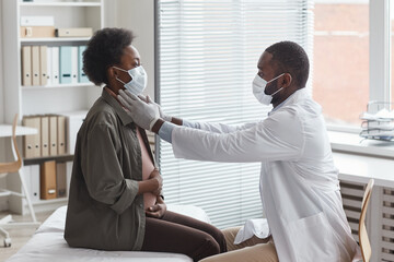 African doctor in protective mask examining pregnant woman during her visit at doctor's office