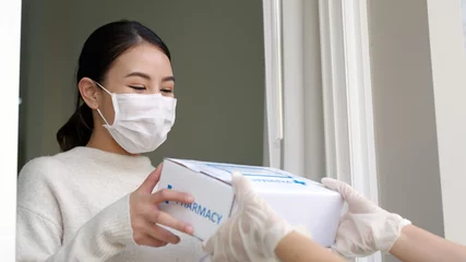 Gordijnen Young attractive beautiful asian female receive medication package box free first aid from pharmacy hospital delivery service at home wear glove, face mask in telehealth, telemedicine online concept. © ChayTee