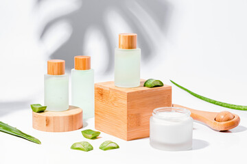 Fototapeta na wymiar Natural cosmetics with aloe on wooden podiums in reusable bottles with plant shadow on background