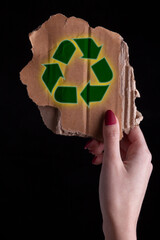 hand holding a piece of  Cardboard With Recycle Symbol - black background