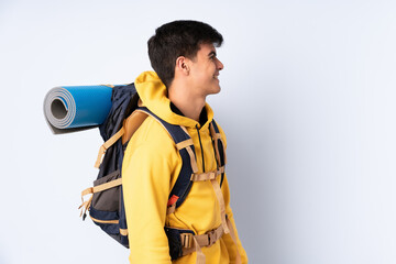 Young mountaineer man with a big backpack over isolated blue background looking to the side