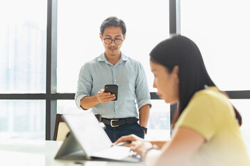 Businessman using cell phone with woman working on laptop in foreground.