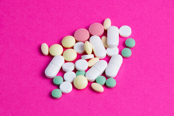 Many multicolored vitamins and pills on a pink background copy space, top view