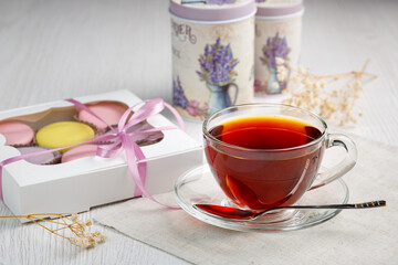 Multicolored macaroons in a box and a cup of tea on a light wood kitchen table. Morning tea and sweets.