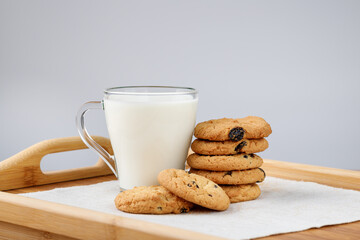 Cup of milk and cookies with raisins on a wooden tray