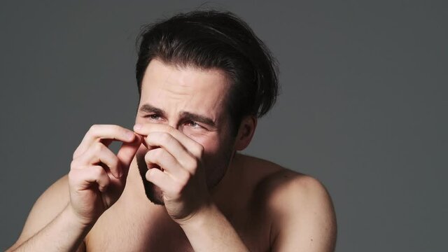 A Displeased Man Is Finding A Gray Hair On His Head Standing Isolated Over Grey Wall In The Studio