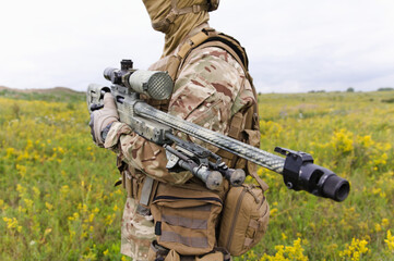 Soldier with sniper rifle standing in blooming green field