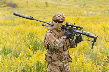 Soldier with big sniper rifle walks across blooming field