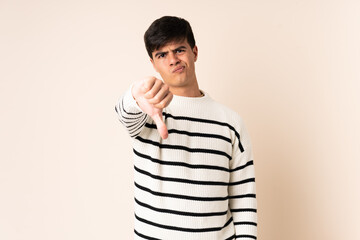 Handsome man over isolated beige background showing thumb down with negative expression