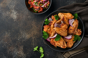Grilled chicken wings or roasted bbq with spices and tomato salsa sauce on a black plate. Top view with copy space.