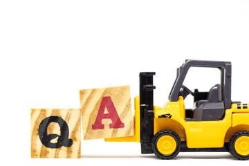 Toy forklift hold letter block a to complete word QA (abbreviation of quality assurance or question and answer) on wood background