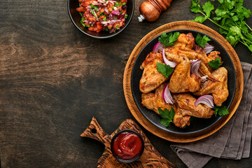 Grilled chicken wings or roasted bbq with spices and tomato salsa sauce on a black plate. Top view with copy space.