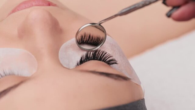 Eyelash extension procedure. Professional beauty master showing results of work in special mirror. Fake eyelashes. Eyelashes extensions close up. Makeup artist and client in beauty salon.