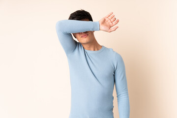 Handsome man over isolated beige background covering eyes by hands