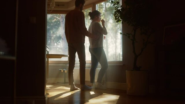 Couple At Home: Woman Watching Out of Window Male Partner Embraces Her From Behind. Happy Couple in Ideal Relationship Spending Sunny Day Together. Beautiful Family Moments