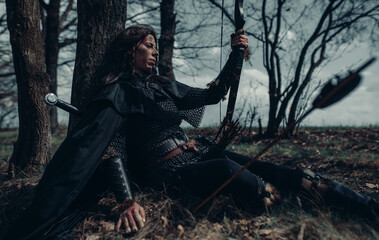 Woman in image of medieval warrior sits and rests in forest.