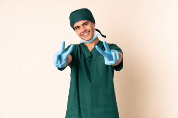 Surgeon man in blue uniform over isolated background smiling and showing victory sign
