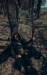 Woman in image of medieval warrior sits and rests in forest.