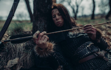 Woman in image of medieval warrior rests and examines her arrow.