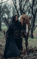 Naklejka premium Woman in image of medieval warrior leads her horse with sword in her hand.