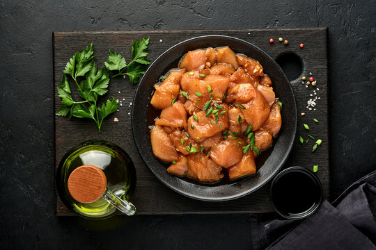 Raw chicken meat marinated in teriyaki soy sauce, onions and pepper in a black plate on a dark slate, stone or concrete background. Top view with copy space.