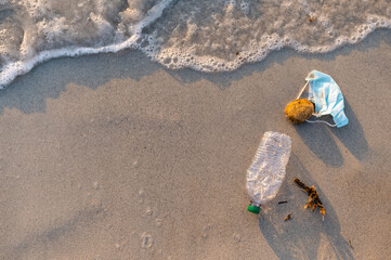 Top view waste on the beach shore. Plastic bottle and face mask. Environmental conservation and...