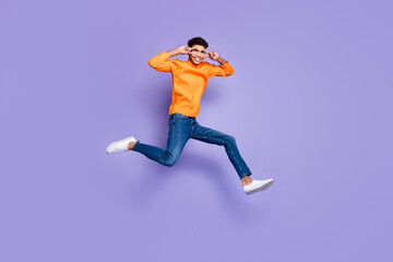 Fototapeta na wymiar Photo of sweet cute dark skin guy dressed orange pullover jumping running v-signs cover eyes isolated purple color background