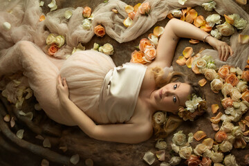 Woman pregnant with child lying amongst flowers and tulle
