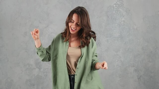 A happy woman dancing while snapping fingers in a gray studio
