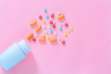 Multicolored tablets, pills, capsules in plastic bottle on pink background, copy space. Heap of assorted various medicine tablets and pills, vitamin and nutritional supplements concept.