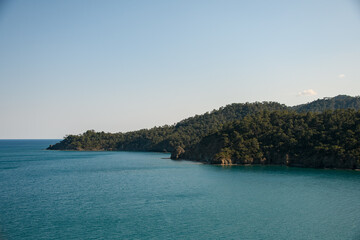 panoramic view of sea on background of mountain ranges with green trees and blue sky