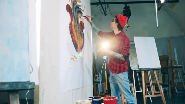Male artist is working on his painting on a massive canvas