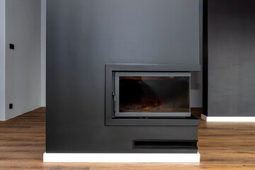 Fototapeta premium A modern standing fireplace in the living room enclosed with panels, painted black with a corner pane covered with soot.