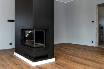 A modern fireplace with a closed combustion chamber standing in the living room, painted black,...