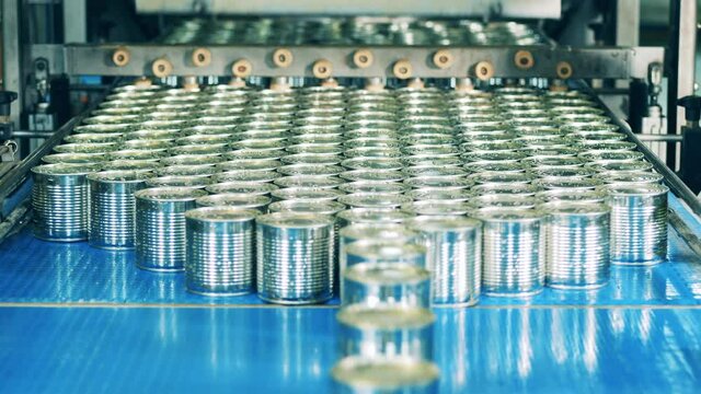 Factory conveyor, industrial production line with metal cans. Batches of newly-sealed tin cans are getting transported