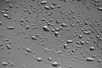 The background and texture of raindrops on the beveled windshield of the car against the grey cloudy sky with blur on parts of the frame in bad weather. High quality photo