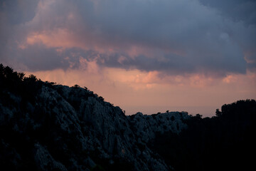 Majestic view on sky and clouds at sunrise. Dark silhouettes of mountains at dawn.