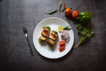 Top view of paneer tikka on a white plate along with salad and vegetable condiments
